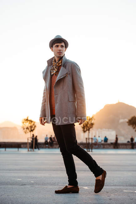 Young trendy man in hat and vintage clothes looking away against mountain on roadway in daytime — Stock Photo