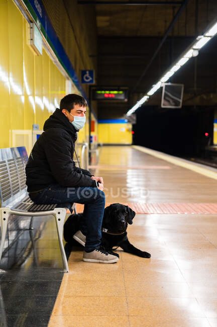 Мужчина в маске с собакой-поводырем на станции метро — стоковое фото