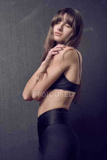 Femme sensuelle avec soutien-gorge tatouage toucher le cou debout en studio sur fond noir — Photo de stock