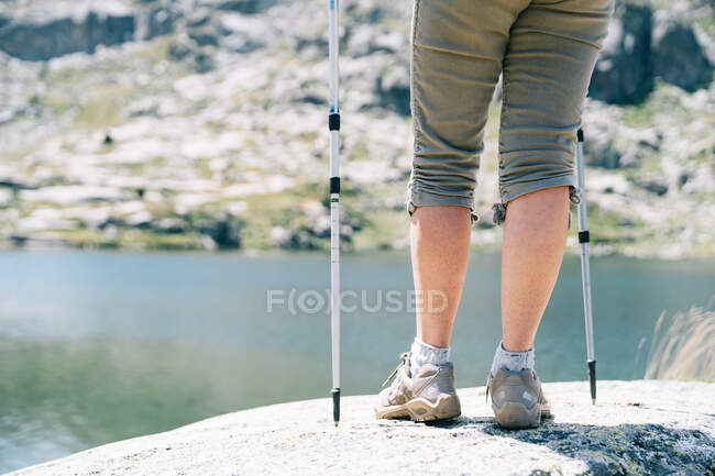 Back view anonymous female hiker standing with walking poles on stony river coast in Catalan Pyrenees on sunny summer weather — Stock Photo