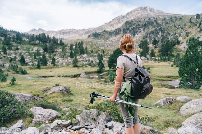 Back view anonymous female hiker in casual clothes with backpack with Nordic walk poles while standing on stony hilltop in mountainous Ruda Valley in Catalan Pyrenees — Stock Photo