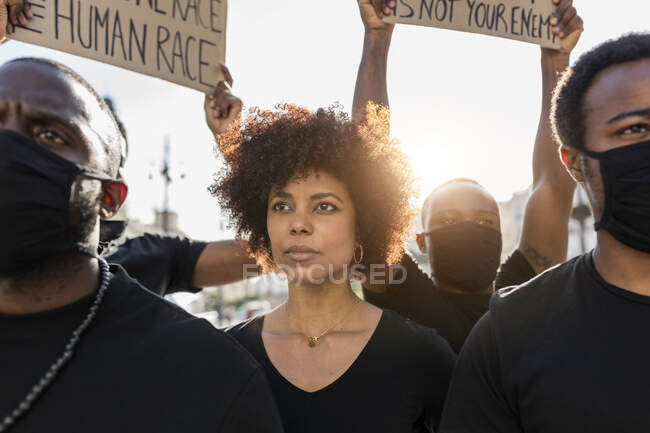 Cultivo anónimos afroamericanos guerreros de justicia social en máscaras durante la manifestación BLM en la ciudad en retroiluminación - foto de stock