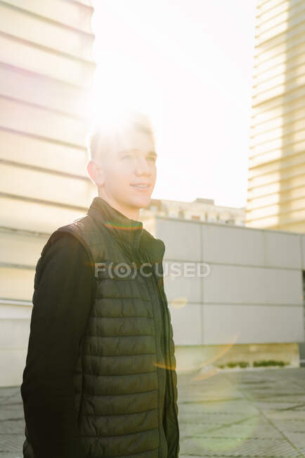 Giovane maschio in abito alla moda in piedi su strada asfaltata e guardando lontano nella giornata di sole — Foto stock