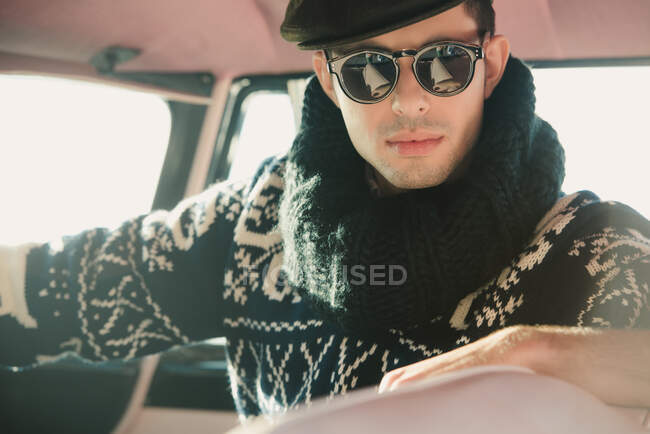 Crop serious male model in soft knitted retro sweater with ornament and collar resting in transport on sunny day — Stock Photo