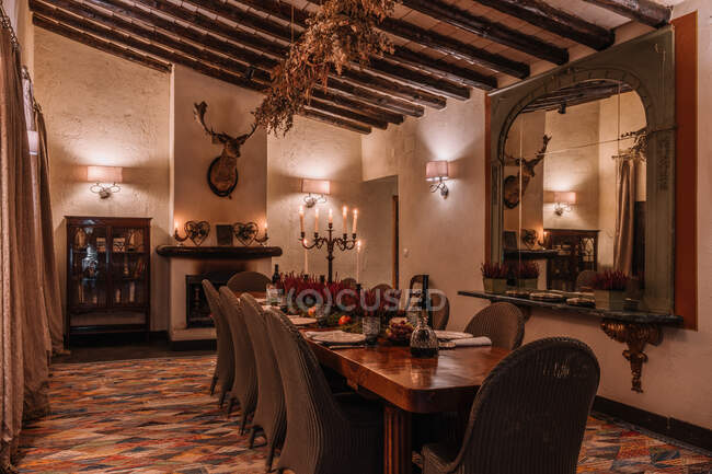Интерьер столовой с деревянным столом со столовыми приборами и тарелками, украшенными цветами на ужин — стоковое фото