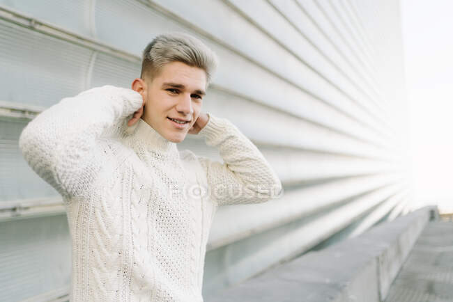 Обличчя молодого стильного чоловіка в модному в'язаному светрі стоїть на вулиці біля сучасних будинків в сонячний день. — стокове фото