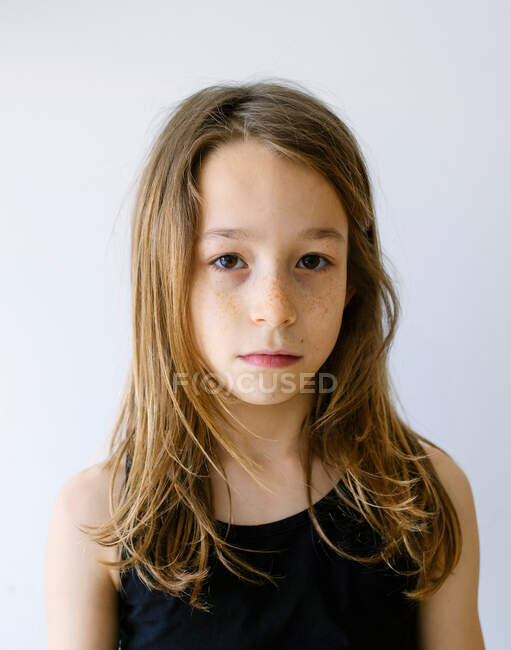 Unemotional ragazza dai capelli biondi in maglietta guardando la fotocamera in piedi sullo sfondo bianco — Foto stock