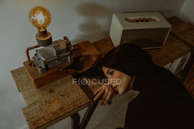 High angle of dreamy female leaning on table in retro room and looking away — Stock Photo