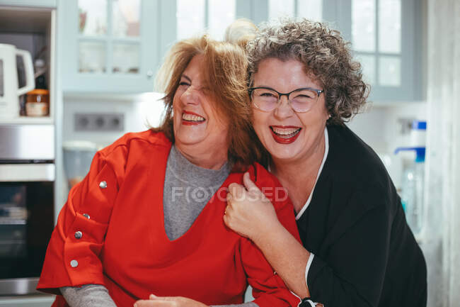Heureuse femme lesbienne d'âge moyen embrassant souriante femme bien-aimée dans la maison — Photo de stock