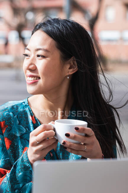Long-haired brunette Asian woman having a coffee on a terrace of a cafe — Stock Photo