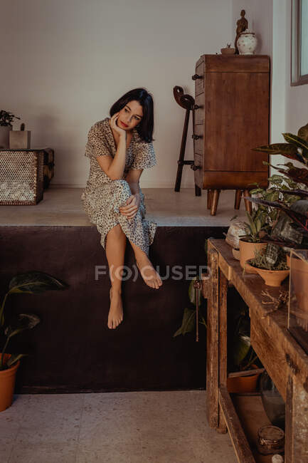 Fêmea delicada no vestido sentado no quarto com várias plantas em vaso em casa — Fotografia de Stock