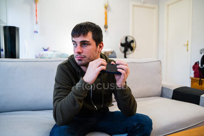 Mann mit Sehbehinderung scrollt Handy, während er zu Hause auf Couch sitzt — Stockfoto