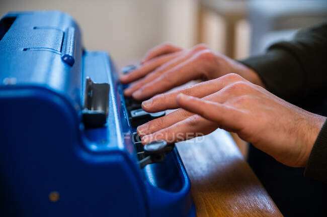 Crop anónimo discapacitado visualmente mecanografía masculina en la máquina de escribir con sistema de escritura táctil en casa - foto de stock