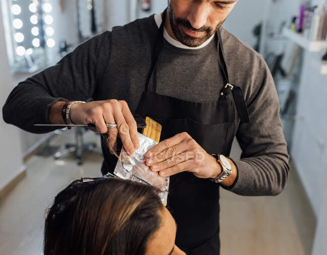 Crop focused ethnic male master combing strands of female customer before dyeing in balayage technique — Stock Photo