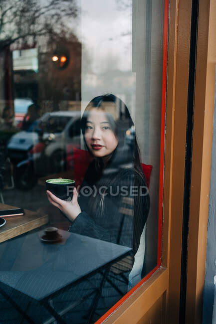 Длинноволосая брюнетка азиатка пьет кофе в кофейне — стоковое фото