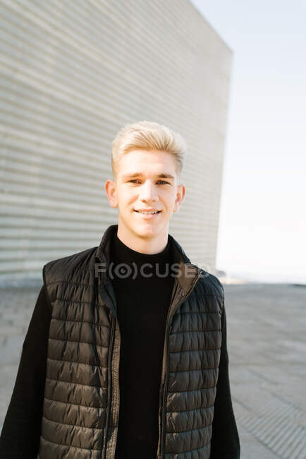 Crop of young male in trendy outfit standing on paved street and looking at camera on sunny day — Stock Photo