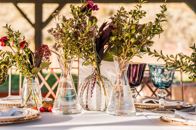 Primer plano de jarrones de vidrio transparente con racimos de flores frescas colocadas en la mesa para el evento - foto de stock