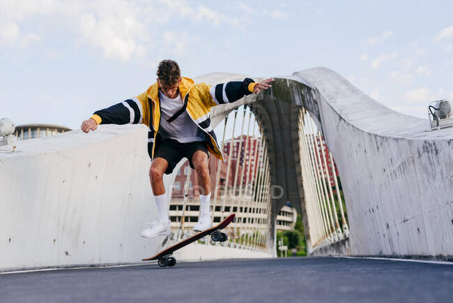 Caucasian teenager jumping with a skateboard in the middle of the bridge in the city — Stock Photo