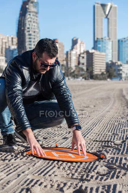 Серьезный мужчина надевает площадку для посадки беспилотников на песчаную почву в солнечный день — стоковое фото