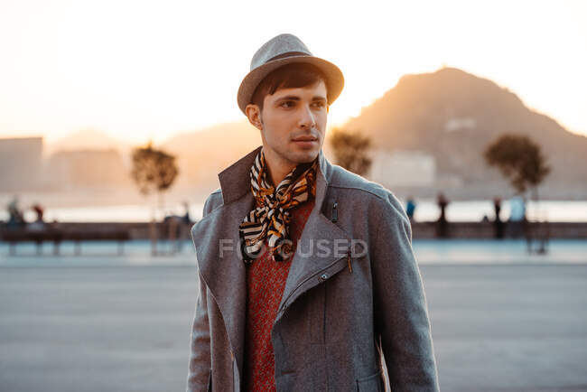 Young trendy man in hat and vintage clothes looking away against mountain on roadway in daytime — Stock Photo