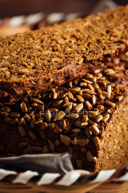 Primer plano de sabroso pan cortado con corteza marrón y semillas de girasol crujientes en la parte superior en canasta de mimbre - foto de stock