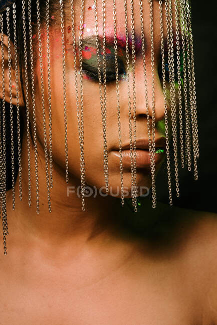 Впевнена етнічна жіноча модель в головній убірці з ланцюжками з закритими очима на чорному тлі в студії — стокове фото