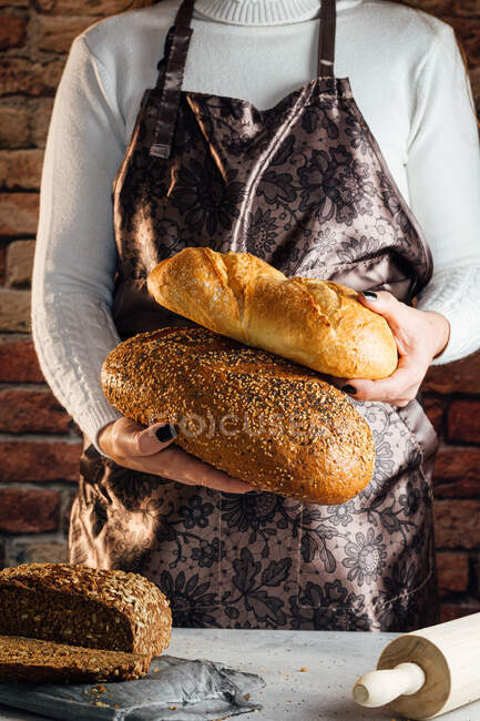 Artista feminina sem rosto em avental com diferentes tipos de pão com crosta dourada e sementes de girassol — Fotografia de Stock