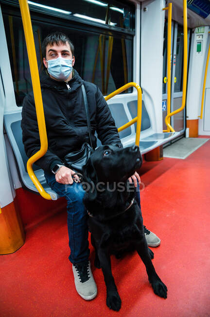 Cuerpo completo de pasajero masculino en máscara médica cabalgando en metro con perro guía - foto de stock