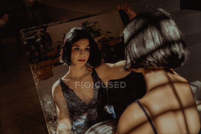 Mulher pacífica sentada olhando para si mesma no espelho retangular no chão no quarto — Fotografia de Stock