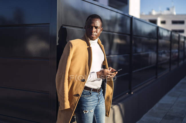 Vista lateral do jovem cara afro-americano sério em roupas elegantes navegando telefone celular enquanto estava no distrito da cidade — Fotografia de Stock