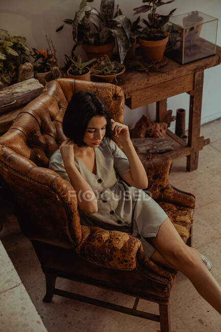 From above of peaceful female sitting in shabby leather chair and touching head while relaxing at home — Stock Photo