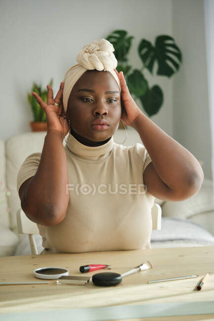 Linda jovem modelo feminino Africano no turbante tradicional elegante sentado na frente do espelho em casa — Fotografia de Stock