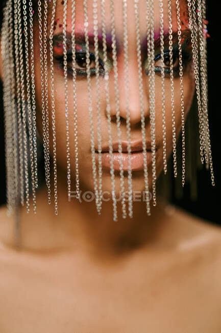 Confident ethnic female model wearing headdress with chains looking away on black background in studio — Stock Photo