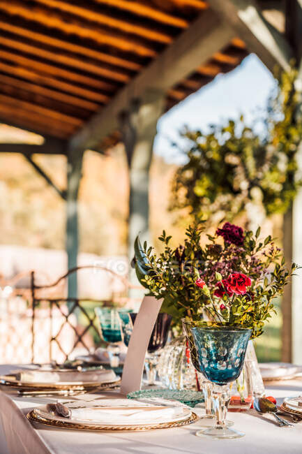 Gros plan de la table de fête servie avec des verres en cristal serviette couverts sur l'assiette près de bouquet de fleurs fraîches pour mariage et carte de menu — Photo de stock