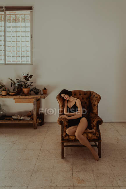 Vista lateral da fêmea pacífica em camisola sentada em poltrona de couro e relaxante com os olhos fechados — Fotografia de Stock