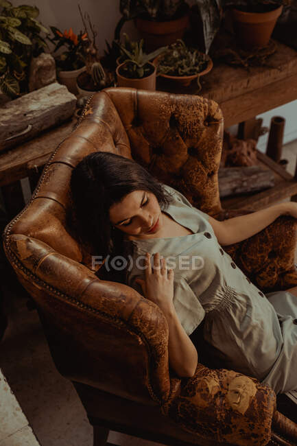 Сверху мирная женщина сидит в потрепанном кожаном кресле, расслабляясь дома — стоковое фото