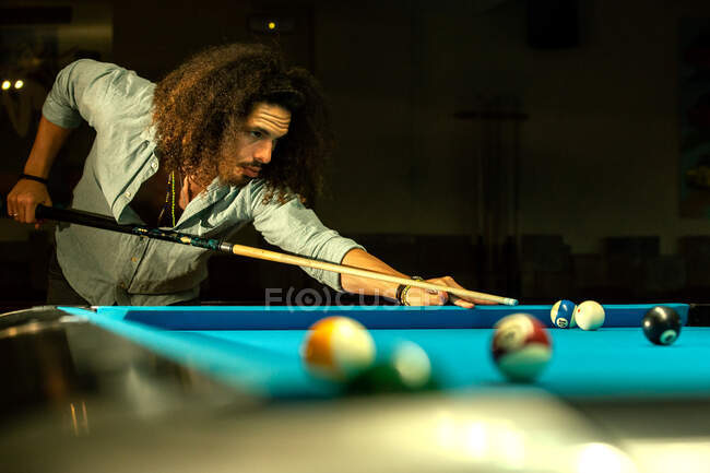 Crop focused bearded male hitting ball with cue while playing game in billiard pool — Stock Photo