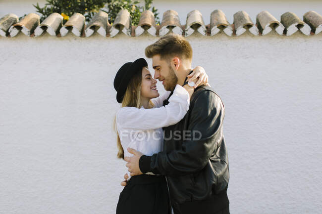 Vista lateral do jovem conteúdo barbudo homem abraçando suavemente alegre namorada enquanto olha um para o outro na cidade — Fotografia de Stock