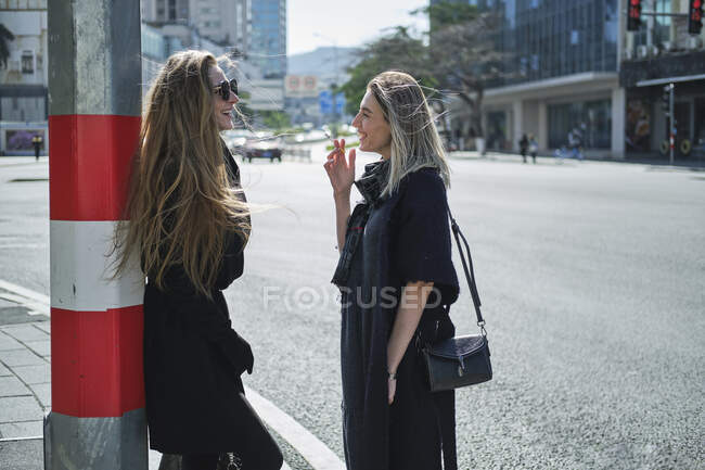 Вид сбоку молодой стильной женщины, которая разговаривает с лучшей подругой, глядя друг на друга на улице — стоковое фото
