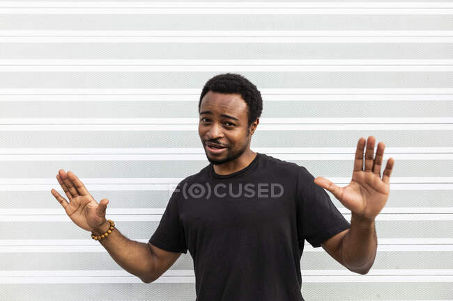 Zufriedener Afroamerikaner in schwarzem T-Shirt steht vor der Kamera auf hellem Hintergrund — Stockfoto