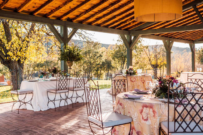 Geräumige Veranda mit Tellern, Gläsern und Besteck auf Tischen mit frischen Blumen für die Hochzeitsfeier — Stockfoto