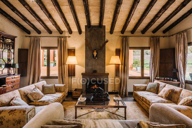 Простора вітальня з диваном і м'якими подушками біля столу і каміну в мисливському будинку — стокове фото