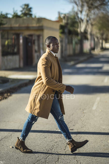 Vista lateral de confiante jovem etnia masculina na roupa da moda atravessando a rua no dia ensolarado — Fotografia de Stock