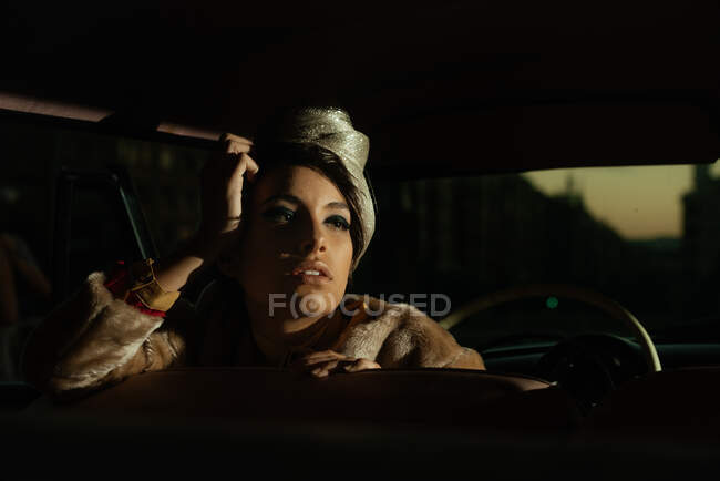 Crop trendy female with flower on hat in automobile while looking away — Stock Photo