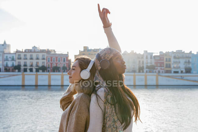Positive multiracial female best friends together from back, enjoying songs with headphones while having fun together — Stock Photo