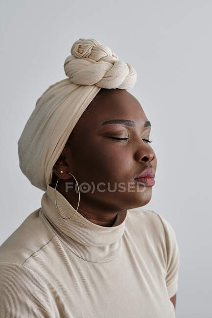 Gorgeous young African female model in stylish traditional turban standing against white background with closed eyes — Stock Photo