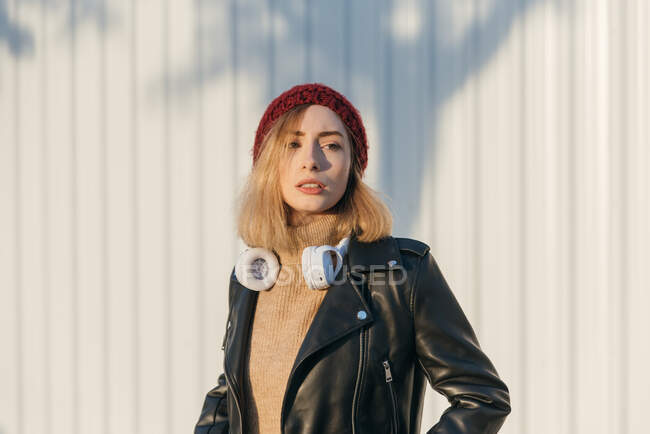 Confident female in street style outfit and with headphone standing in urban area and looking away — Stock Photo