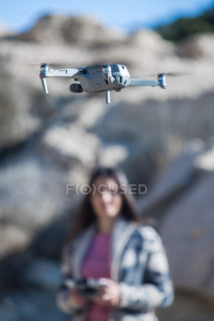 Verschwommenes, unkenntliches Weibchen mit Fernbedienung, die in der Natur steht und oberirdisch fliegende Drohnen bedient — Stockfoto
