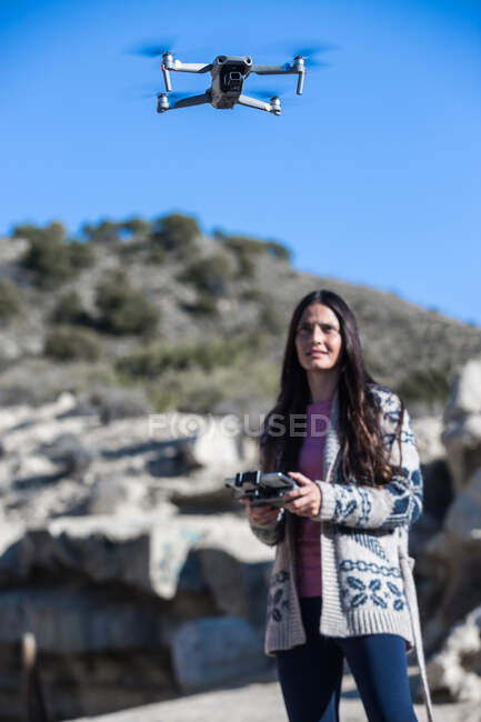 Donna sorridente con telecomando in piedi in natura e drone volante operativo fuori terra — Foto stock