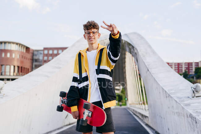 Adolescente caucasiano de pé com um skate no meio da ponte na cidade — Fotografia de Stock